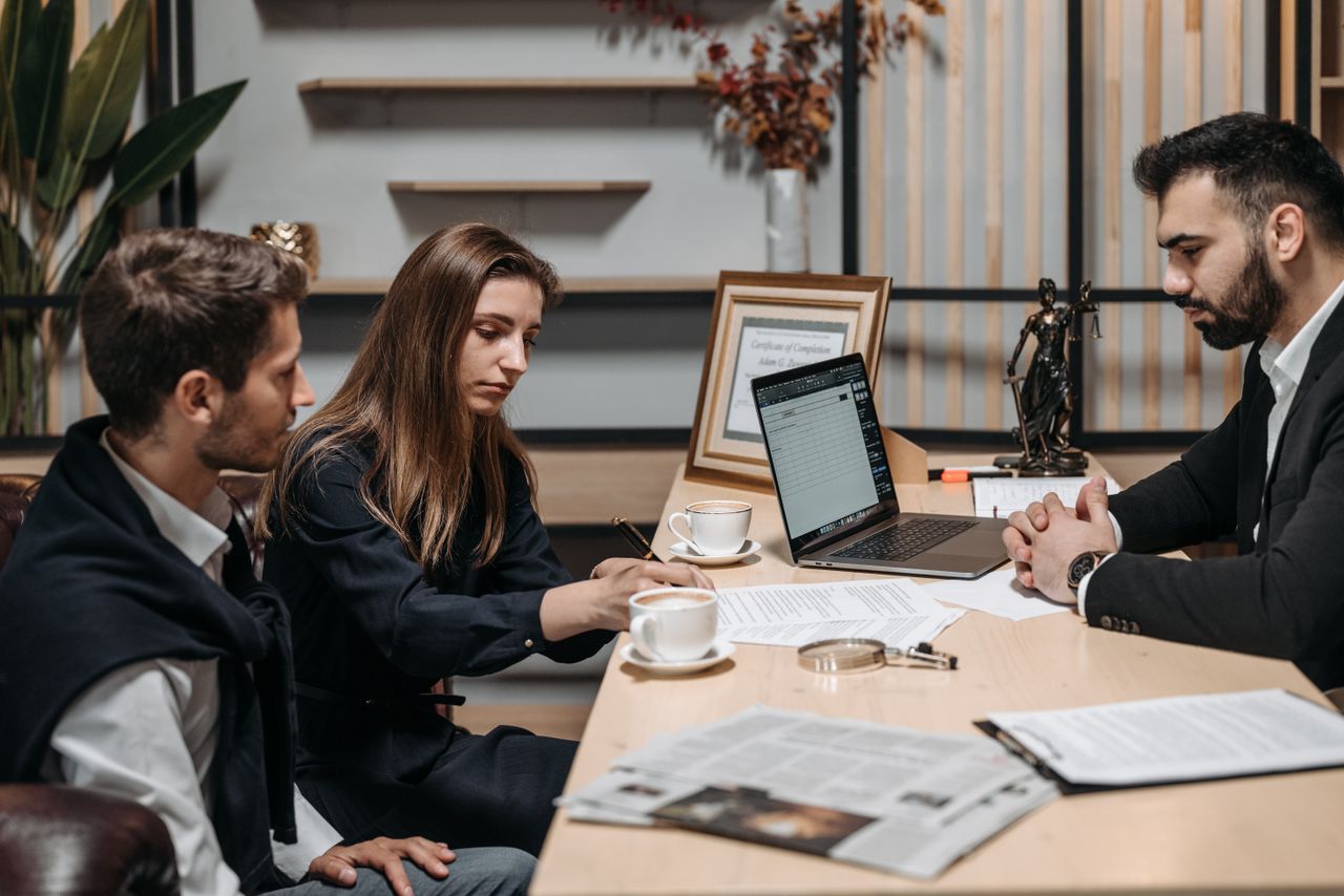 class-02 Three professionals discussing documents over coffee in a modern office setting.